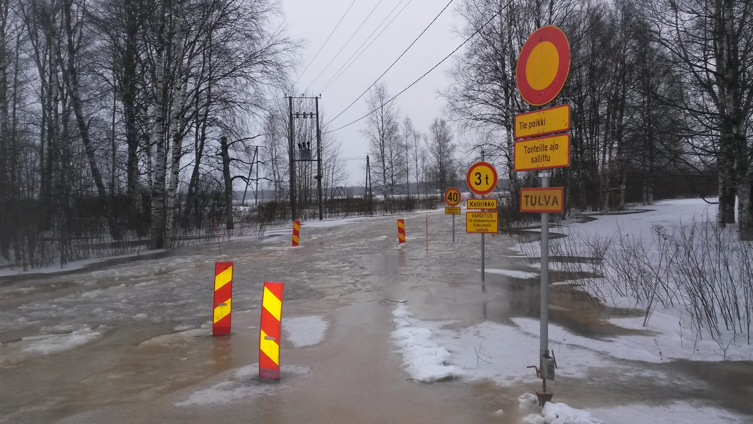 Kuvituskuva vuoden 2018 hyydetulvasta. Kuvassa on noussut vettä tielle ja tien varressa on varoituskyltti tulvasta.