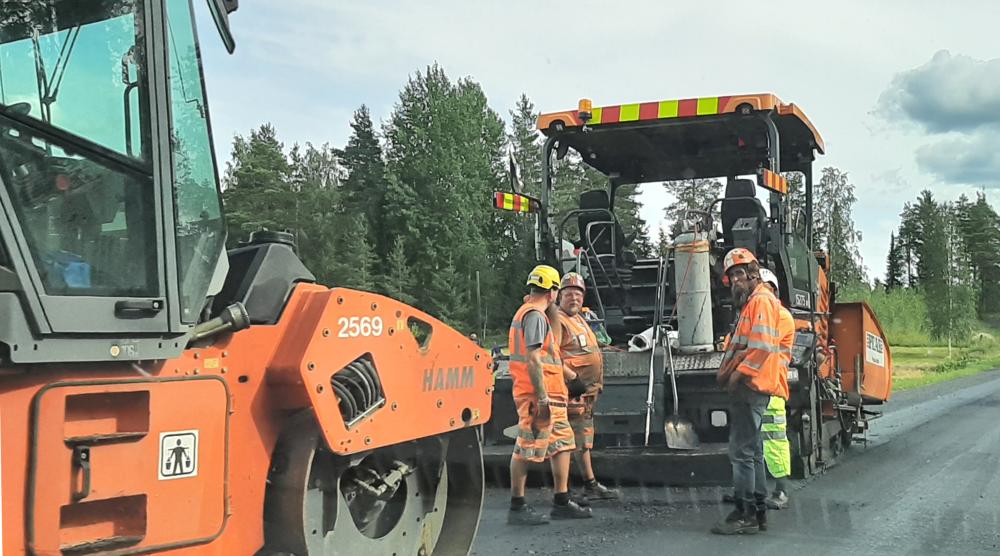 Päällystemiehiä seisomassa tiellä ajoneuvon vieressä. 
