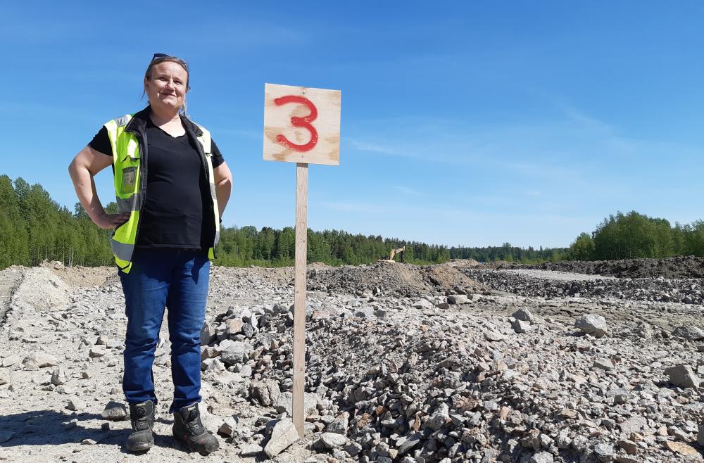 Mirka Kamarjanskij seisoo numerotaulun luona. Työmaata näkyy takana.