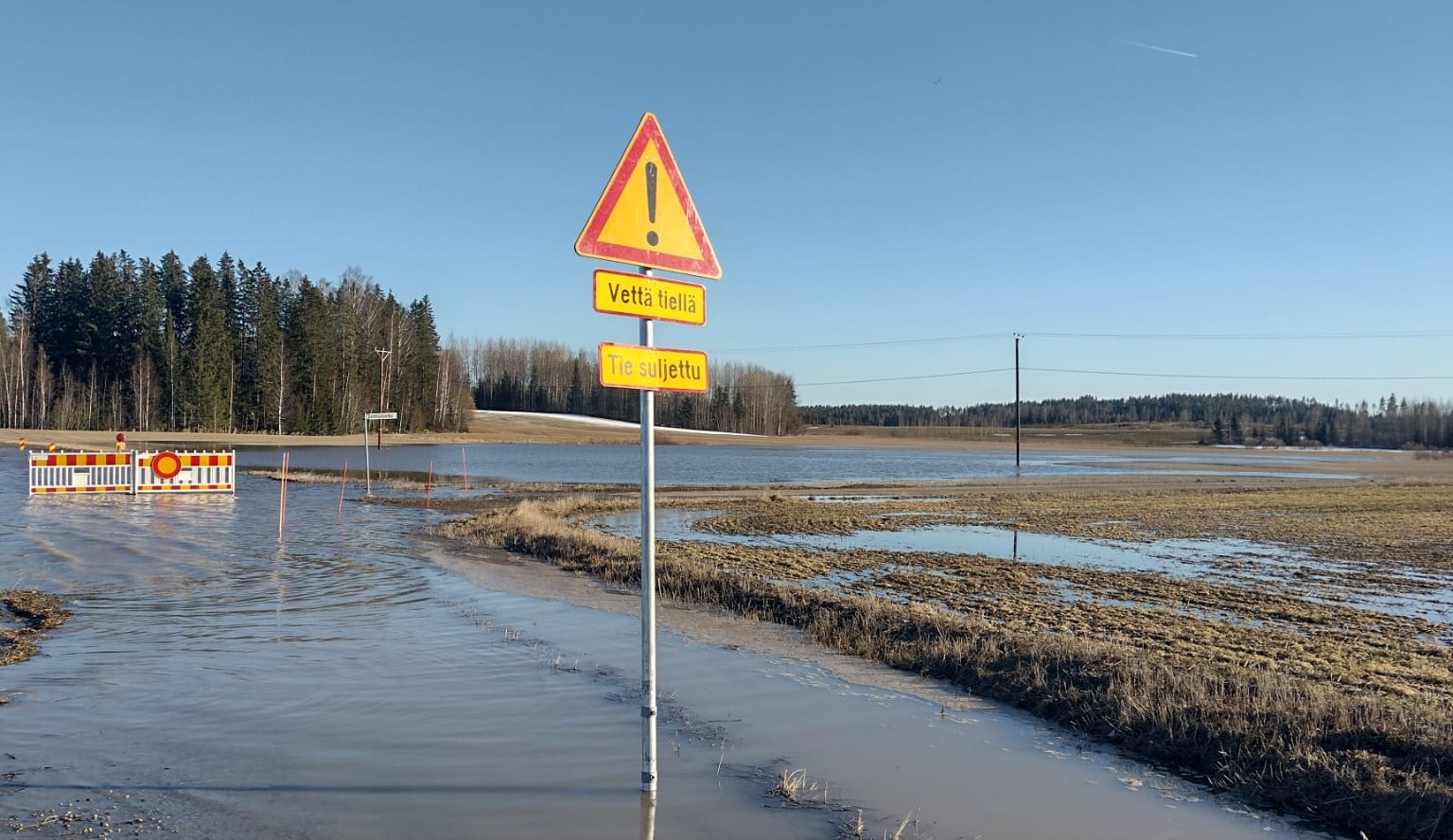 Tulviva pelto ja kyltti, jossa lukee "vettä tiellä".