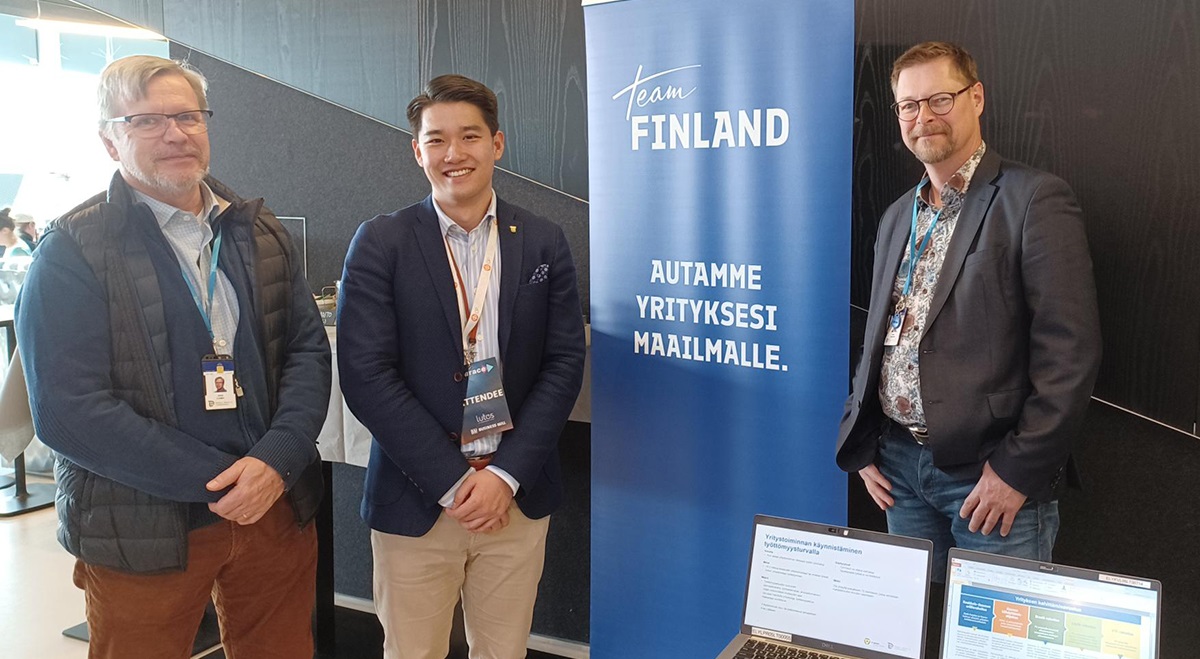 Kolme miestä seisomassa vierekkäin ja takana on Team Finlandi roll up. 