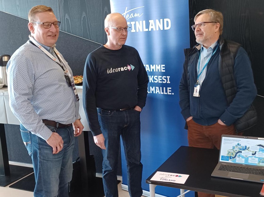 Kolme miestä keskustelemassa keskenään messuosastolla ja takana on Team Finlandin roll up. 