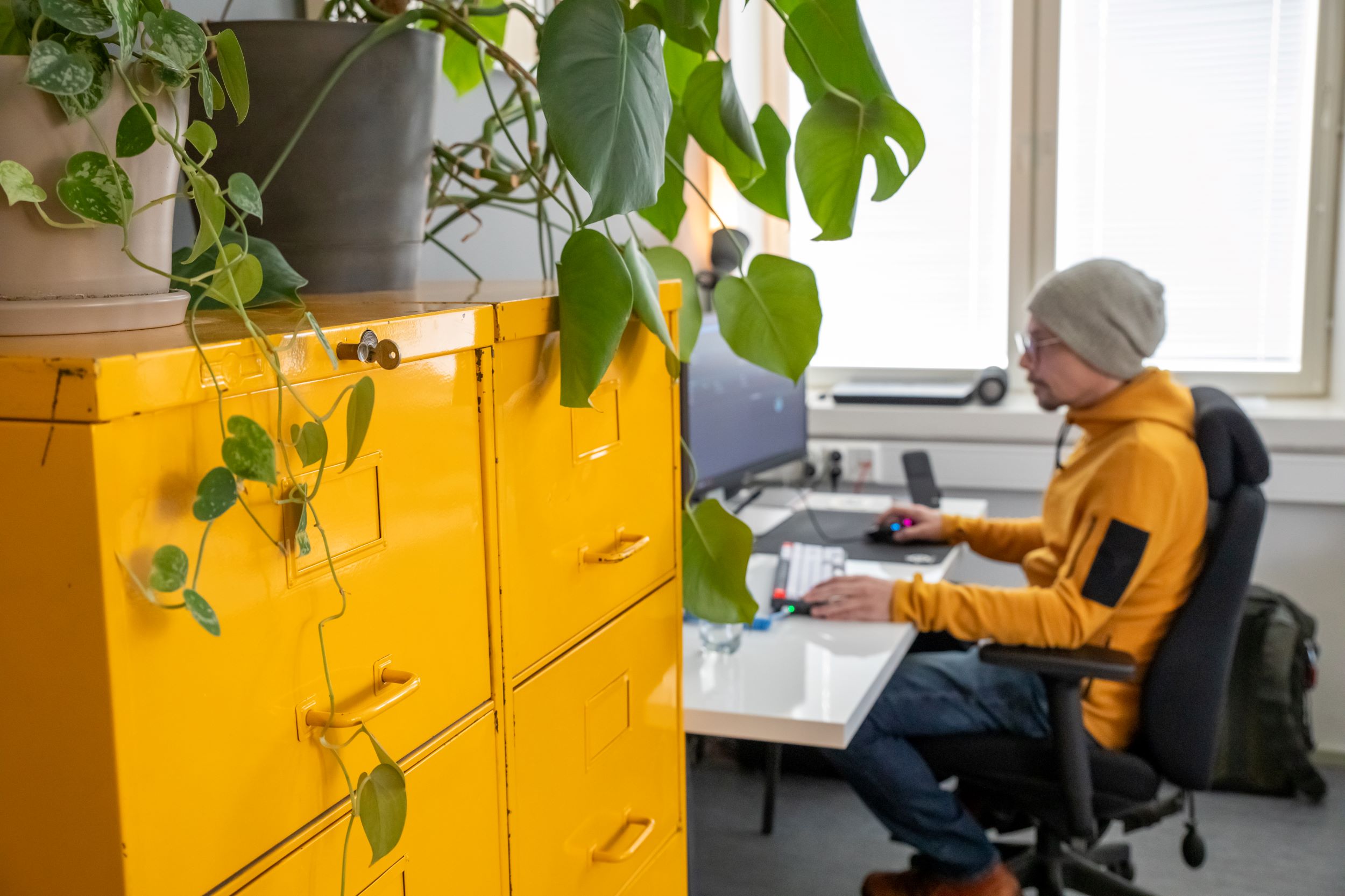 Ensemblen toimistolla keltaiset metallikaapit ja taustalla henkilö työskentelee tietokoneella.