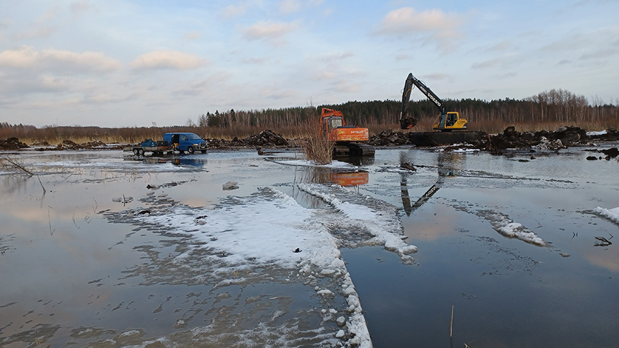 Talvinen jäinen järven kunnostustyömaa, jossa työkoneita ja ajoneuvo.