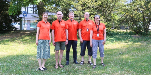 Viisi ihmistä seisoo puistossa ELY-keskuksen edessä oransseissa paidoissa.
