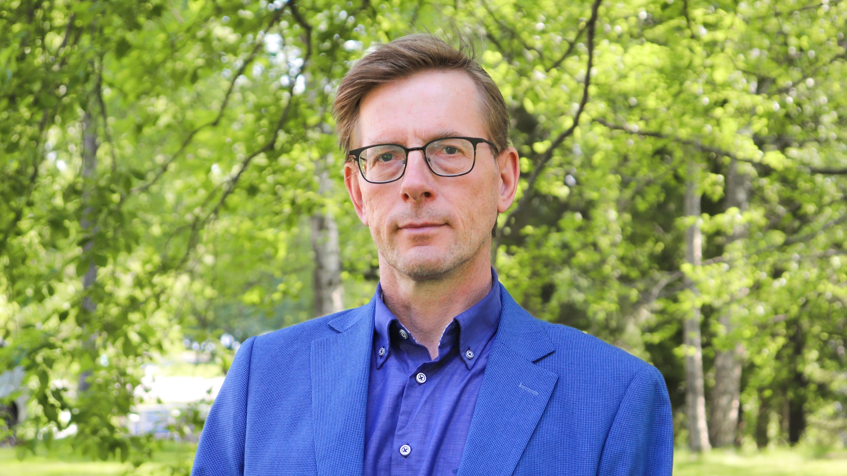 Juha Nummela seisoo puistossa sininen puku yllään