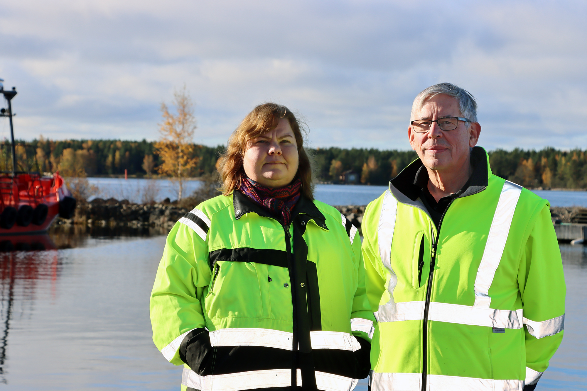 Sirkku Rönkä ja Mikael Åbacka seisovat vierekkäin. Taustalla näkyy merta Kaskisten satamassa ja ruskaista metsää.