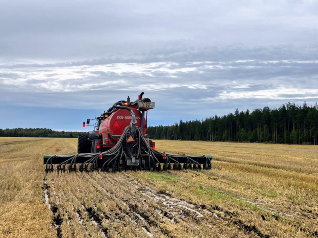 Takaa kuvattu traktori, joka levittää pellolle tärkkelyslietettä multaavalla kiekkolevittimellä syksyllä.