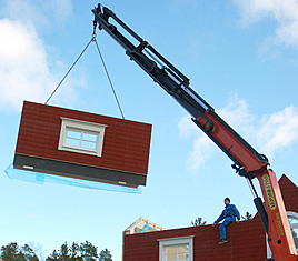 Illustration: en kran lyfter en del av huspaketet.