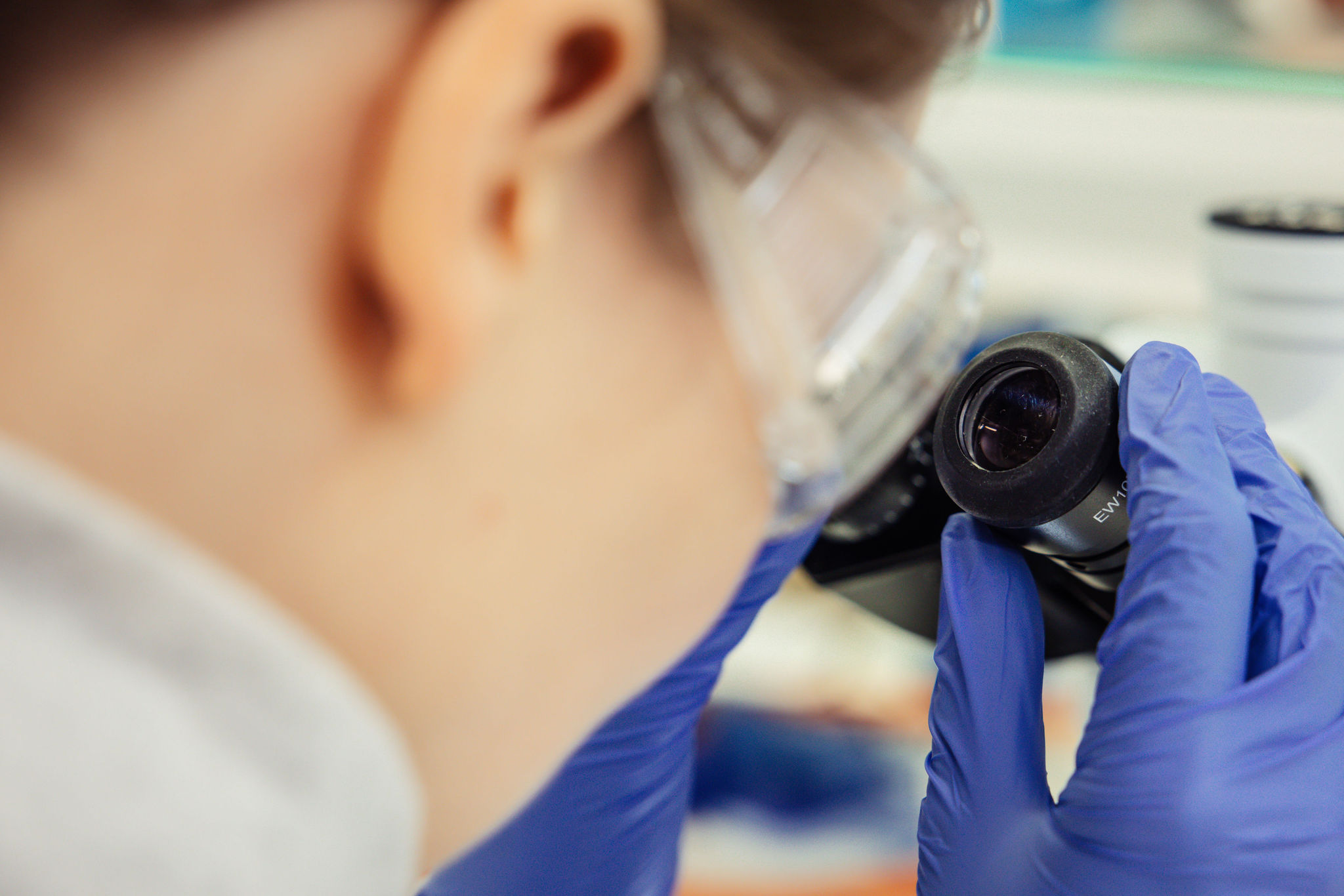 Ihminen katsomassa kiikareita suojalasit ja suojakäsineet päällään. 