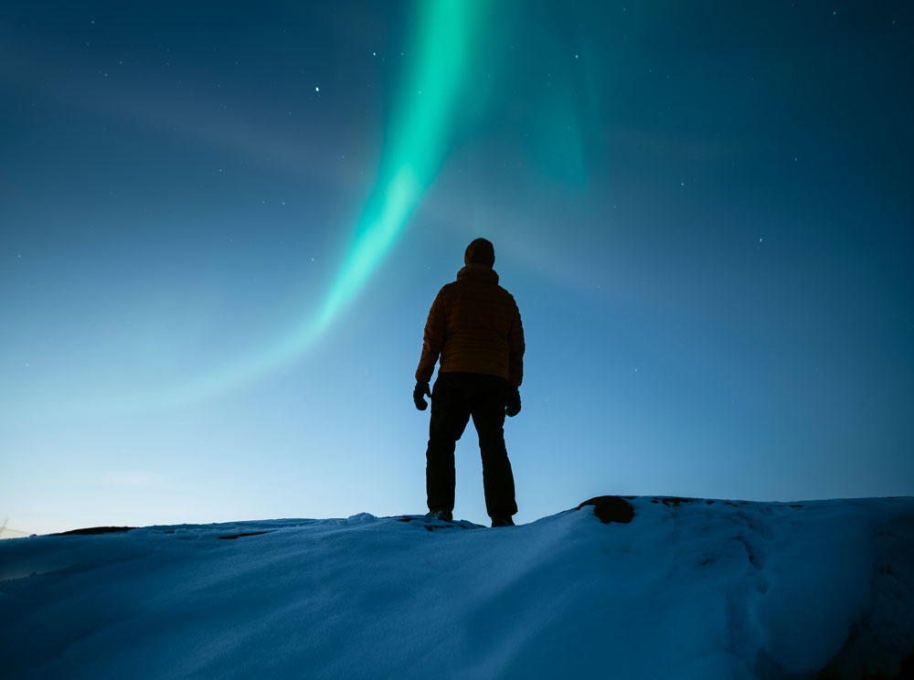 Talvimaisemassa revontulia ja ihminen.