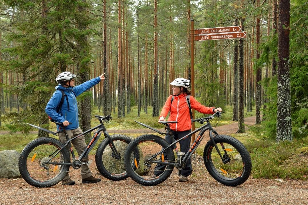 Mies ja nainen pysähtyneinä sähkömaastopyörillä kangasmetsäisessä maastossa.