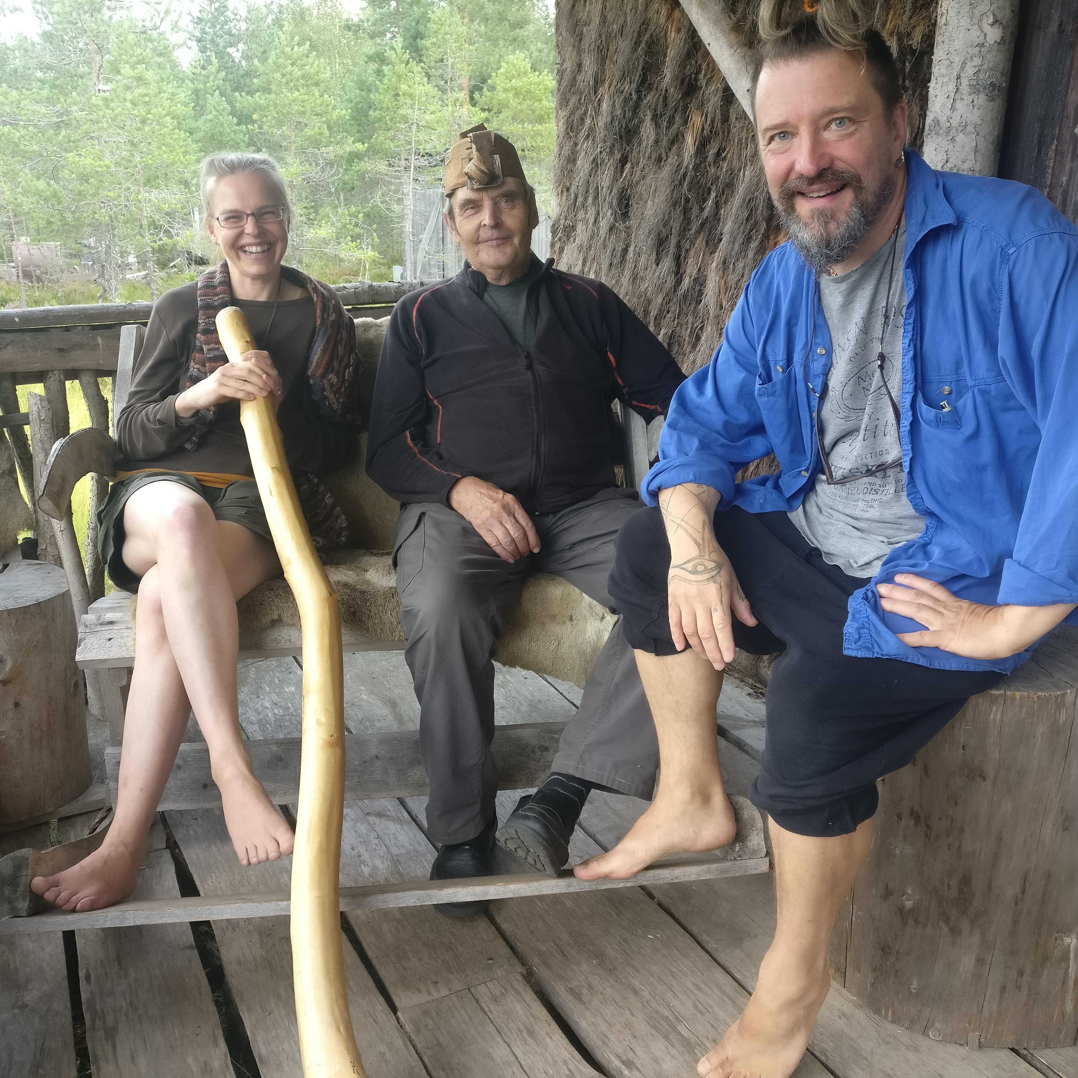 Saila Reiniö, Erkki Kalliomäki ja Mikki Paajanen istumassa penkeillä Kammikylän savusaunan terassilla.