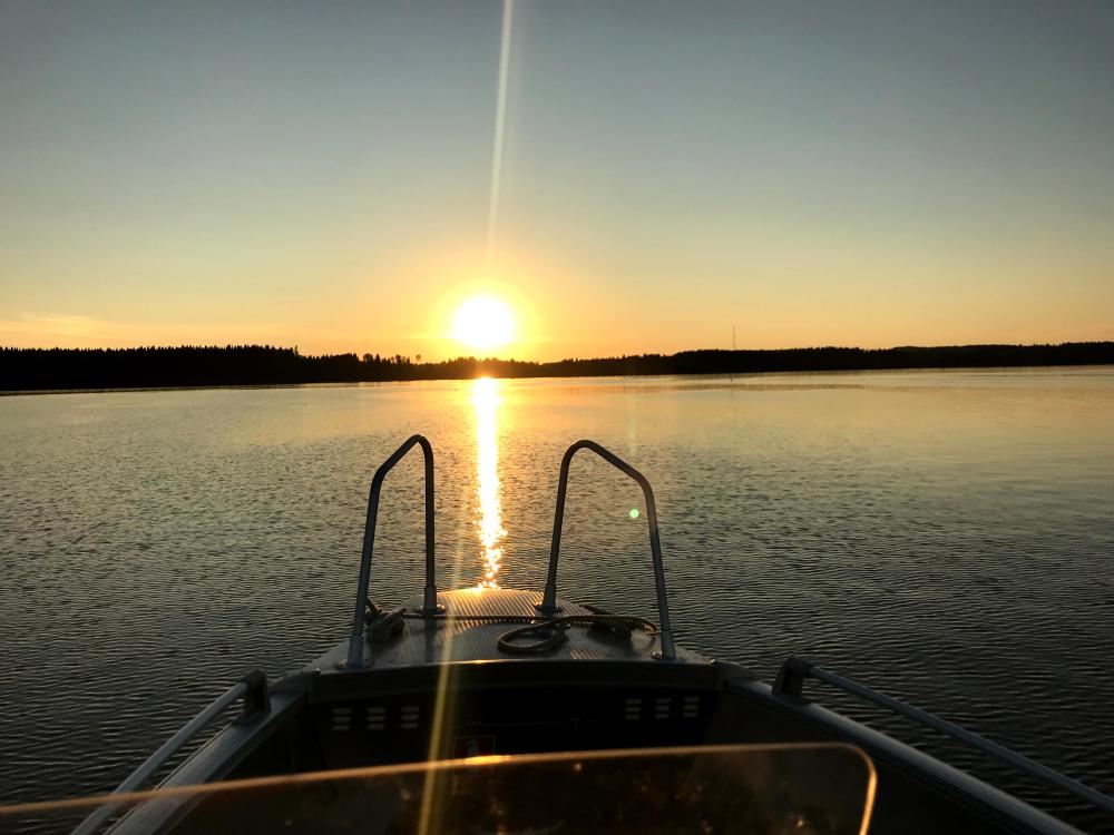 Kuva, jossa veneen keulan läpi näkyy auringonlasku järvellä