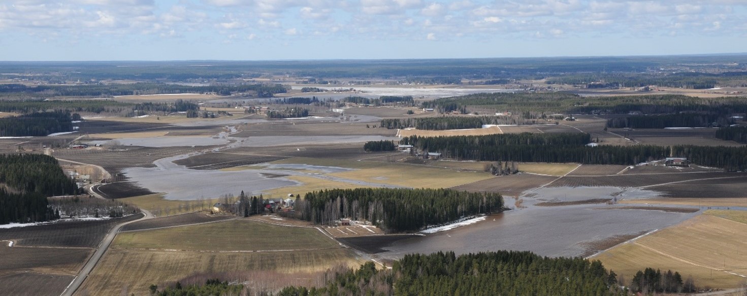 Maisema, jossa metsää, peltoa ja vettä.