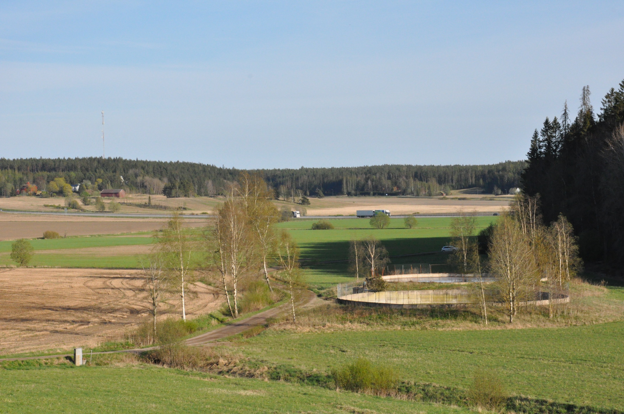 Ett fältlandskap med två landningsbassänger i mitten. På höger sida av fälten finns en skog och motorvägen syns i bakgrunden.
