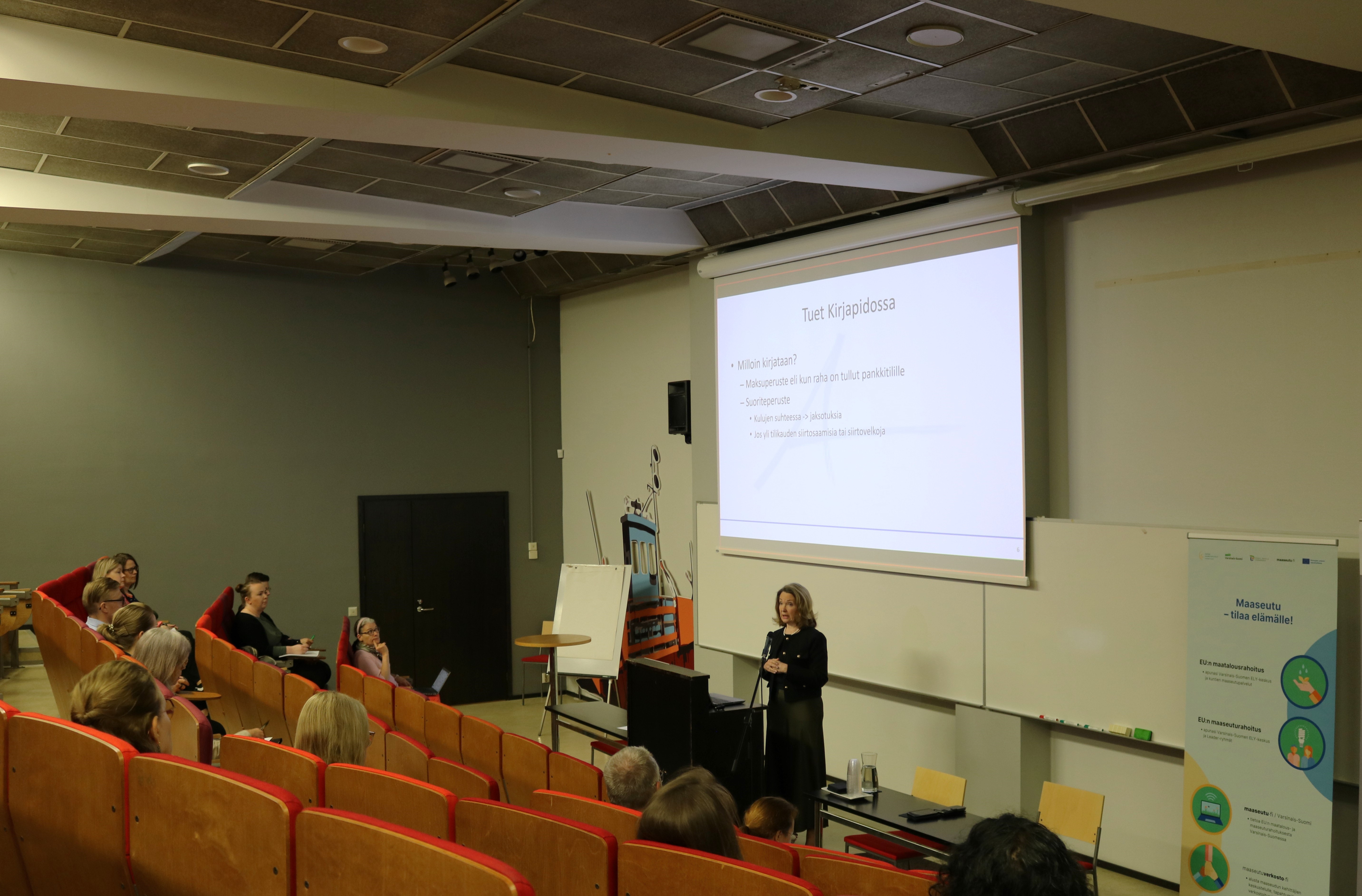 Henkilö auditorion edessä pitämässä puheenvuoroa.